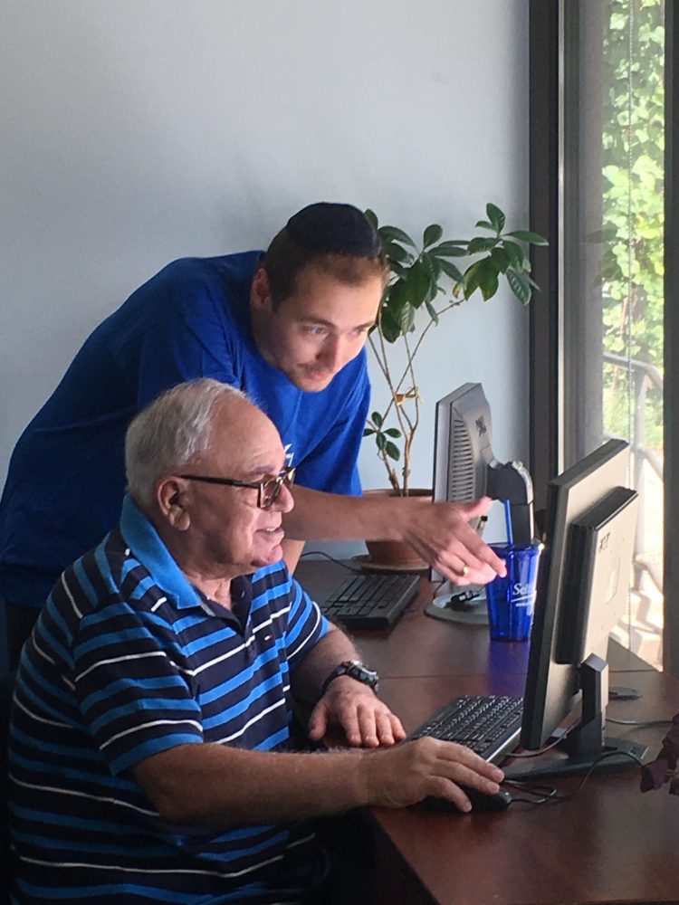 young man helping elderly man use a computer